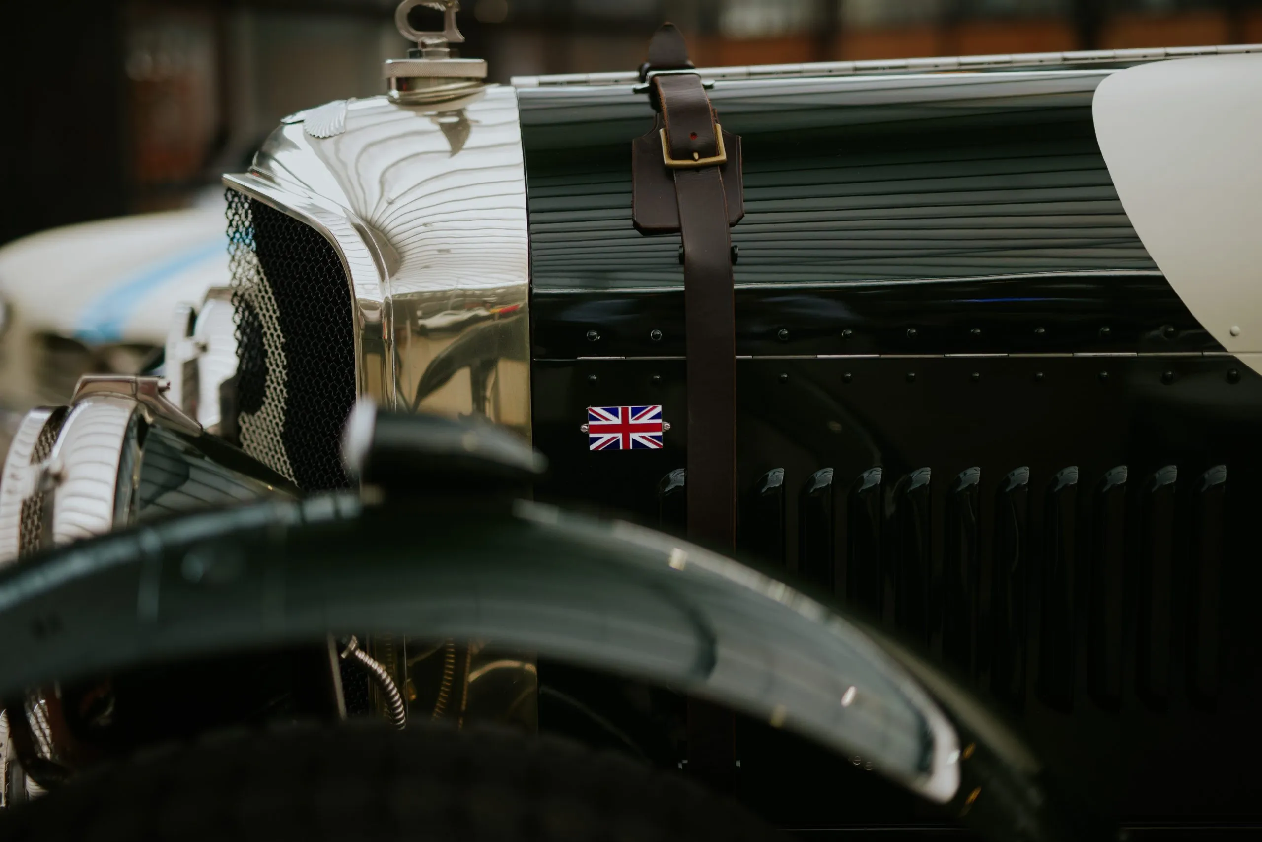 Close-up of a vintage British racing car, a leather strap across its dark green bonnet