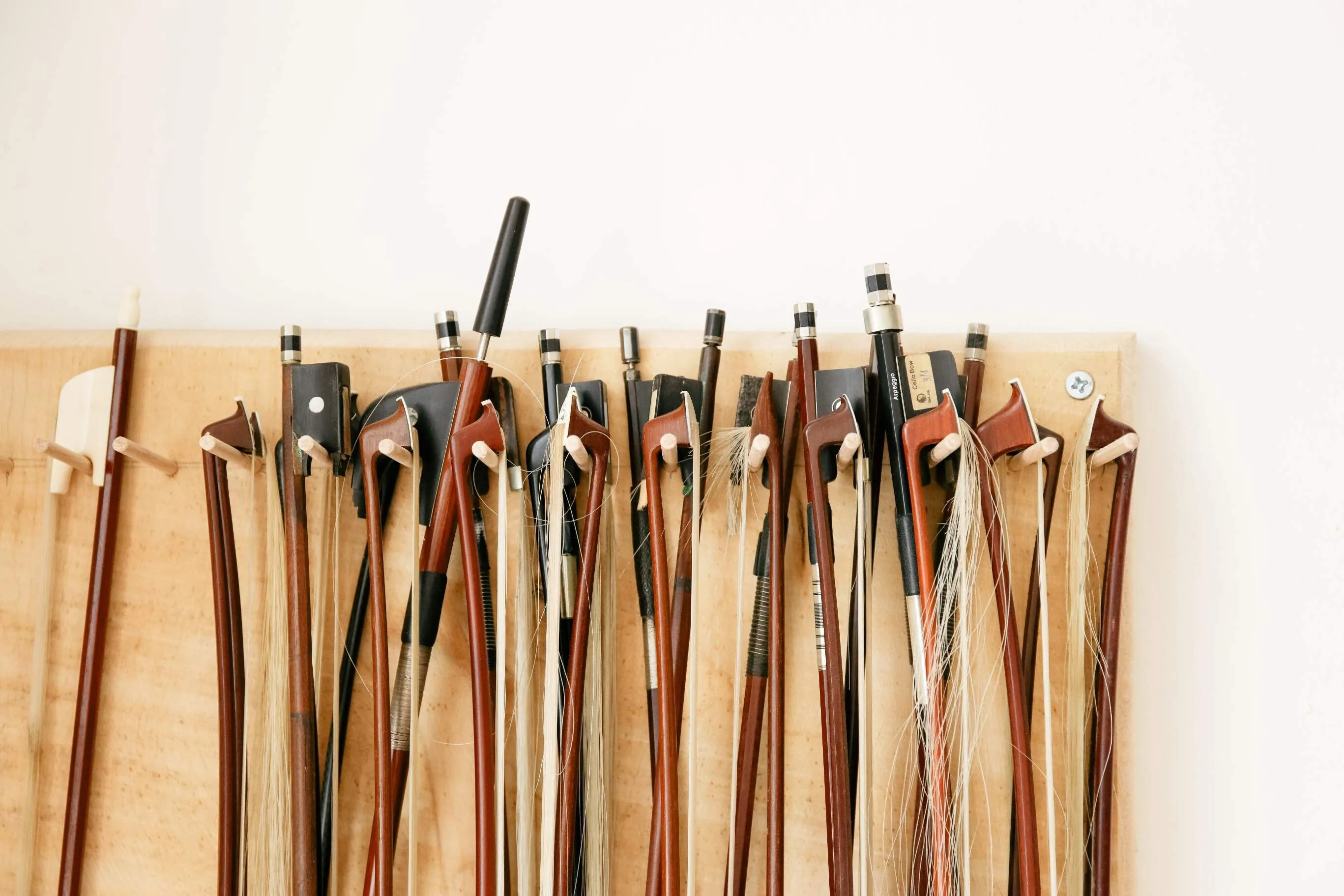 A row of violin bows with frogs and horsehair hanging on a wooden board